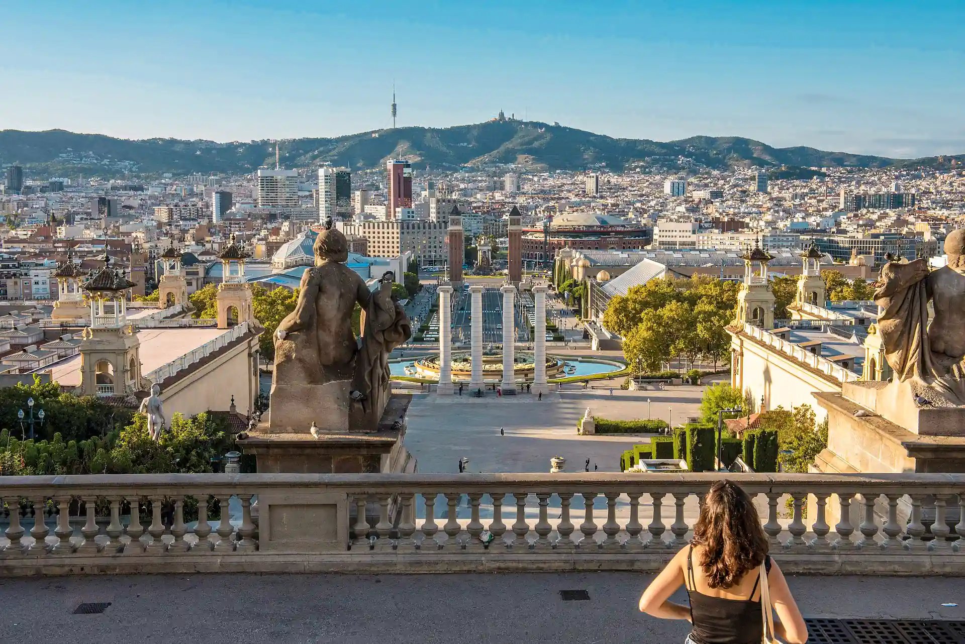 Ein Panoramablick über Barcelona aufgenommen vom Dach des Museu National d'Art de Catalunya. Auf dem Balkon ist eine Person zu sehen welche sich die Aussicht ansieht.