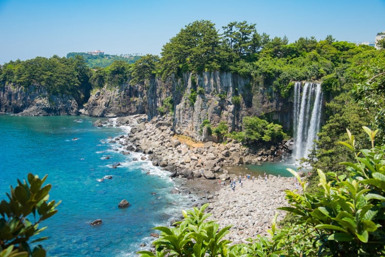 Panoramablick auf die Insel Jeju und einen Strand mit Wäldern und Klippen sowie schönen Wasserfällen und kristallklarem blauen Wasser