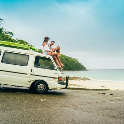 AIFS Australien: Gruppe erlebt Abenteuer am Strand mit Auto, Bully, Surfbrett und Meer – Entdecke mit AIFS Educational Travel unvergessliche Reisen.